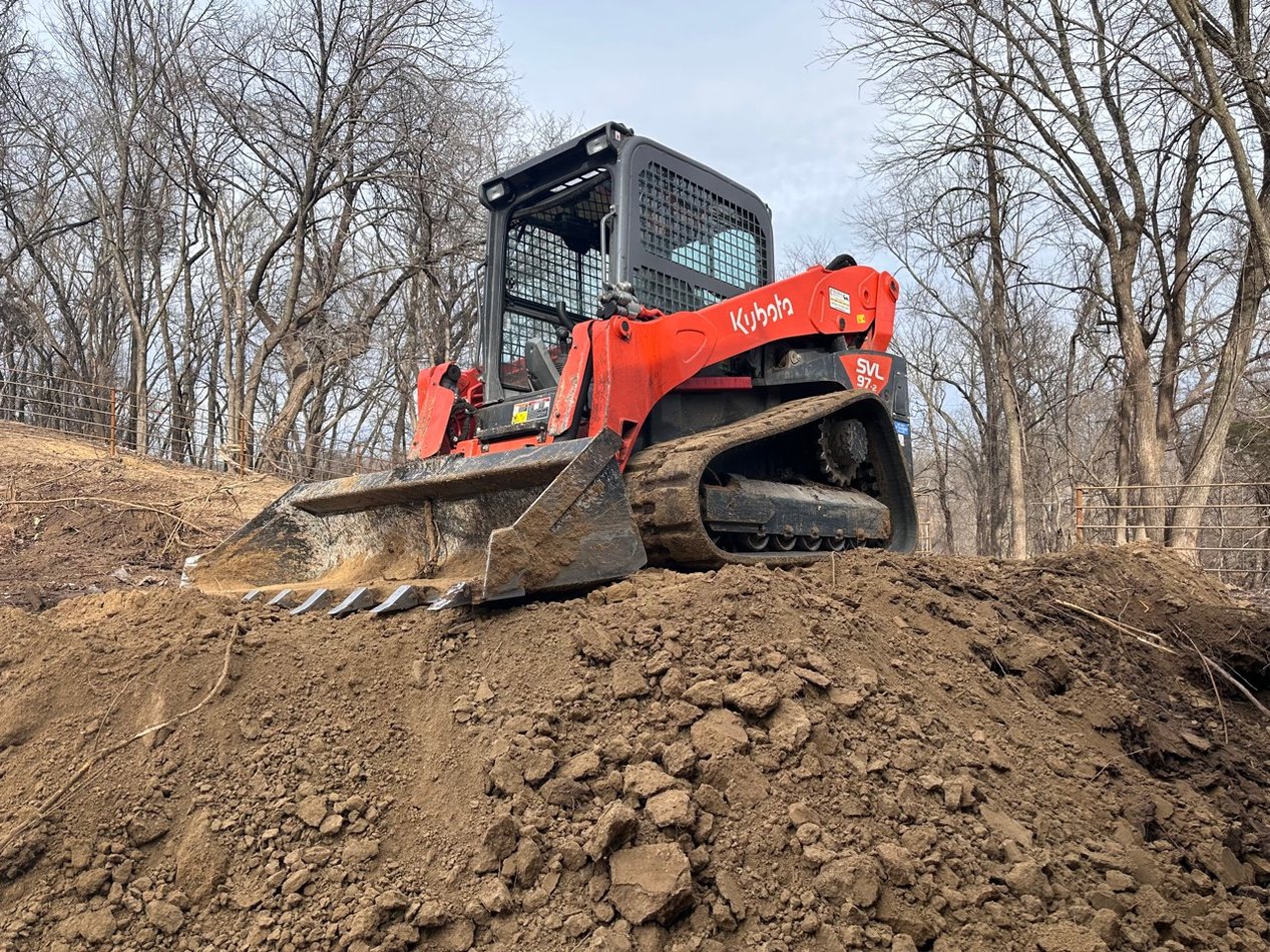 Compact loader performing dirt work on a wooded property