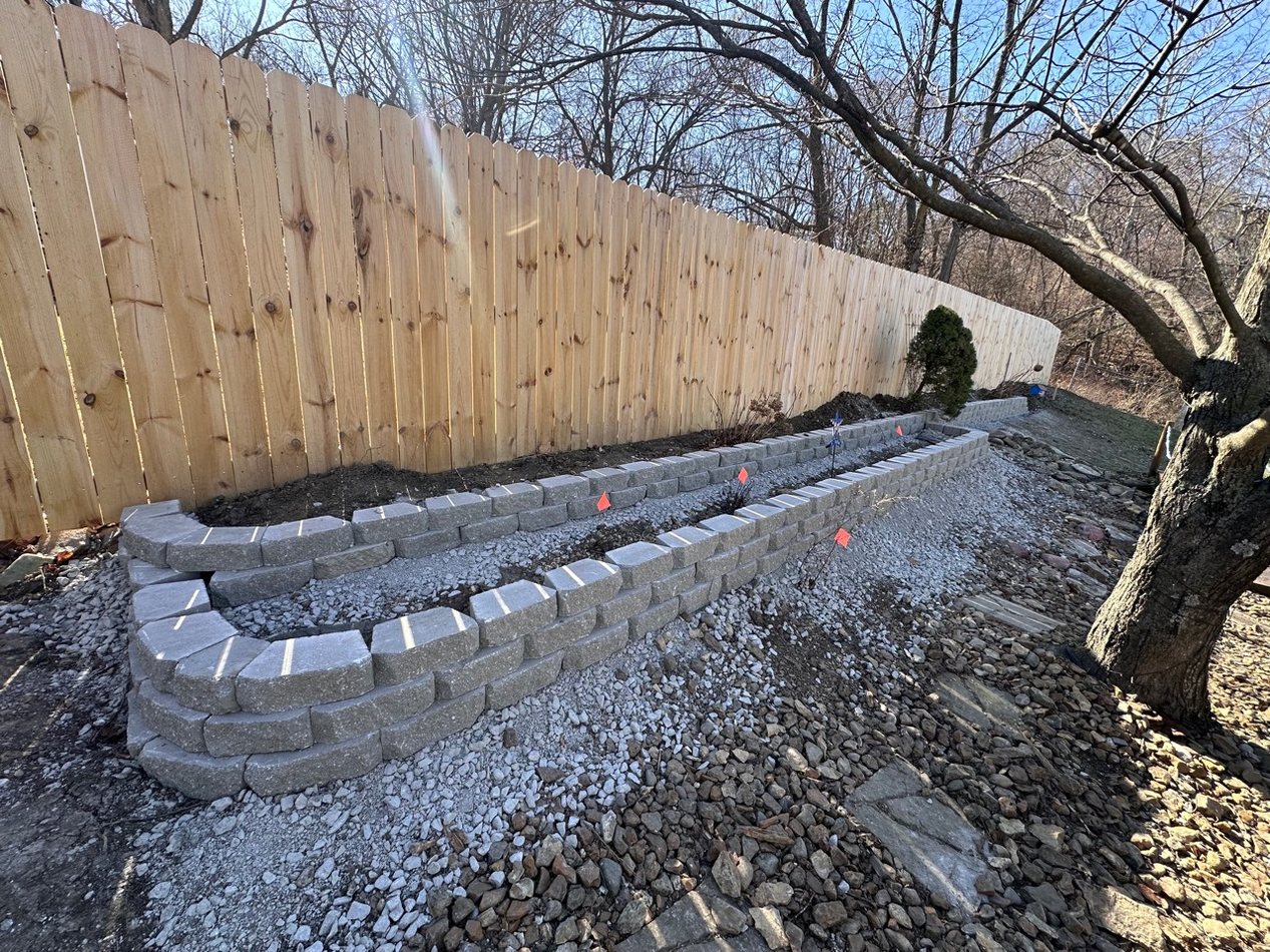 New retaining wall installation beside a wood privacy fence